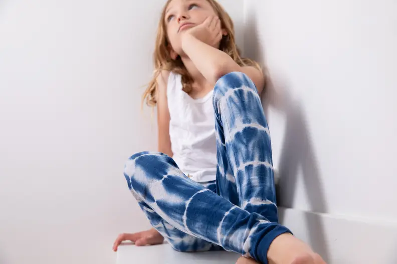 A girl wearing a pair of blue tie dye pants sits cross legged