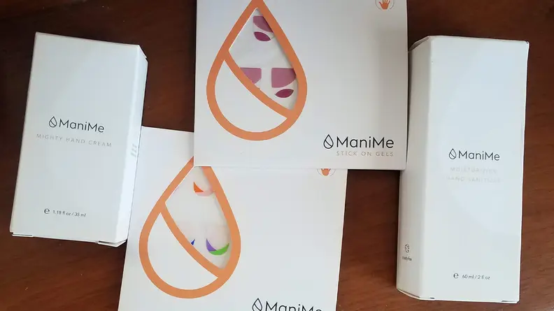 The two nail kits the author received from ManiMe laying on a wooden table and a sanitizer and hand cream from the brand.
