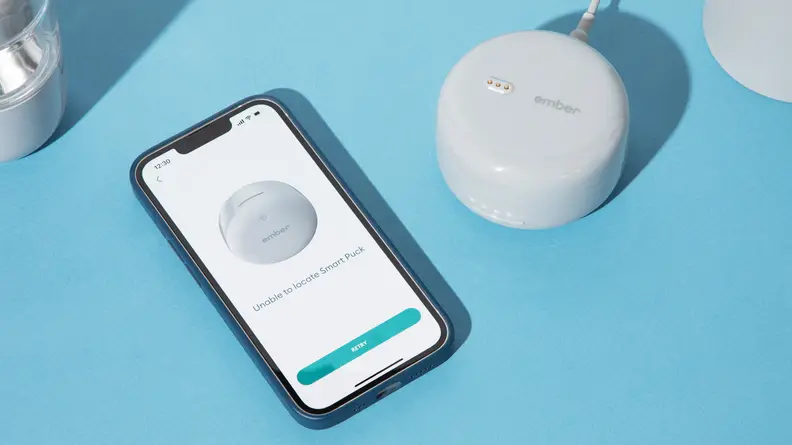 The Ember Baby Bottle System next to a smart phone on a blue background.