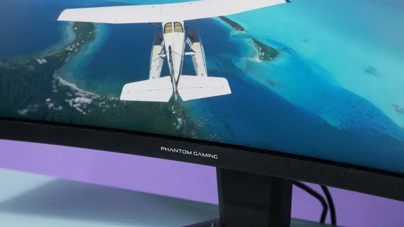 A plane flies over a bright blue lagoon on the screen of an ASRock Phantom Gaming PG34WQ15R2B monitor.