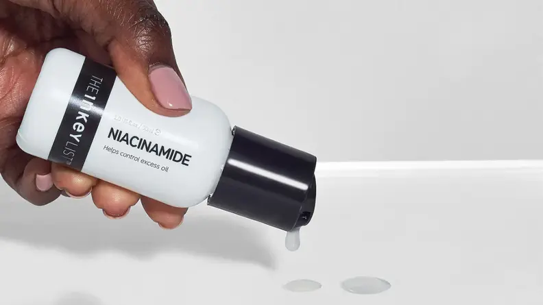 A hand tipping a small white bottle of serum with product spilling out.