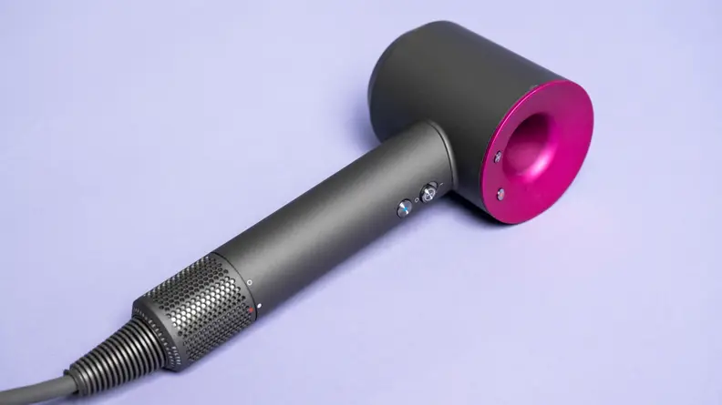 A charcoal gray and fuschia hair dryer laying on a light purple background.