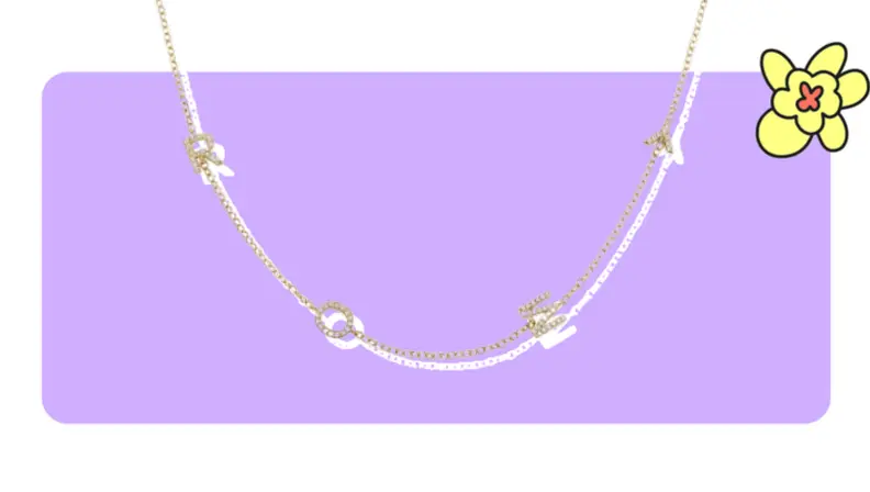 A gold pendant necklace with diamond-crusted letters in front of purple background with a yellow cartoon flower in the corner.