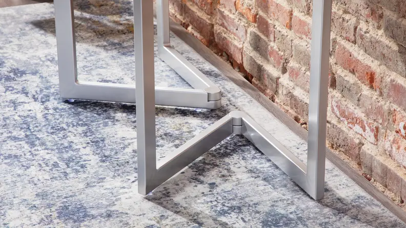 The metal legs of the Expand Furniture Mini Flip shown against a brick wall with a blue carpet underneath