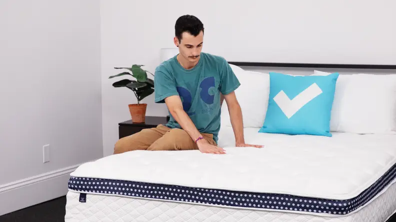 Person sitting on top of a WinkBed hybrid mattress and using hands to feel bed's material.