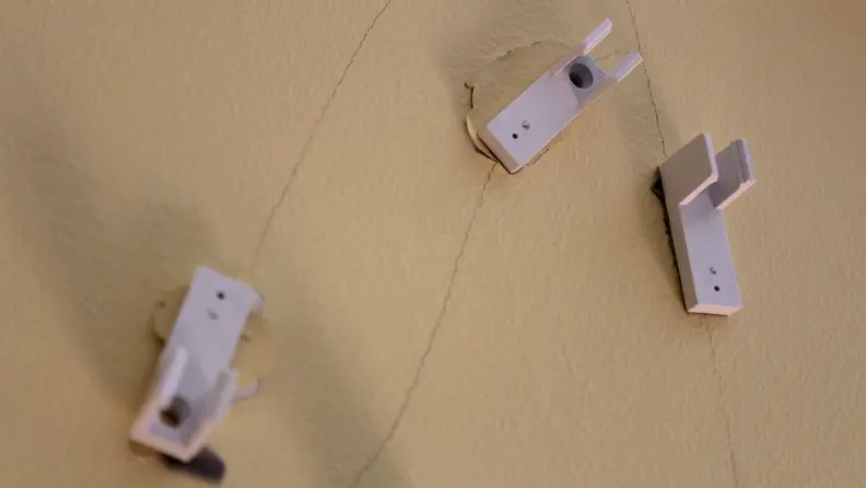 Three small, white wall mounts for lights stuck on tan damaged wall.