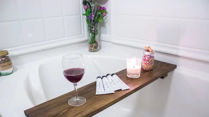 Wooden tray with wine glass, lotions, candle and porporri placed over bath tub
