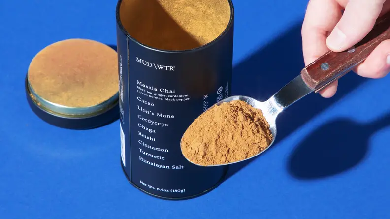 A person getting a scoop of Mud/Wtr powder out of a blue Mud/Wtr container.