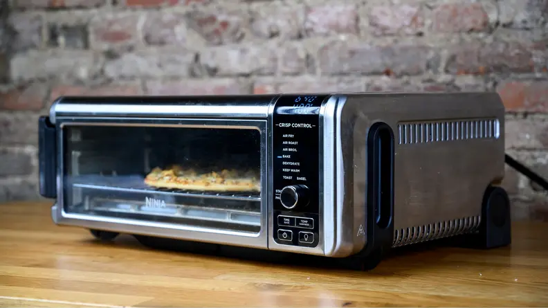 A Ninja Foodi oven sits on the counter cooking a pizza.