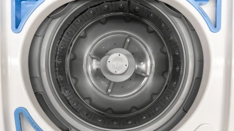 A close-up of the Frigidaire FFTW4120SW washing machine's stainless steel drum. In the top left, top right, and lower left corners of the image, you can see the detergent, fabric softener, and bleach trays arranged around the drum's opening.