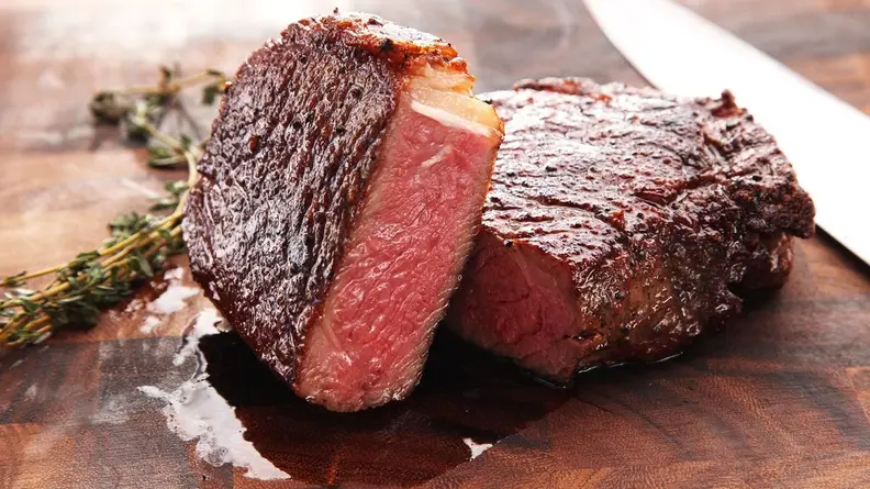 A piece of steak cut in half on a wooden cutting board