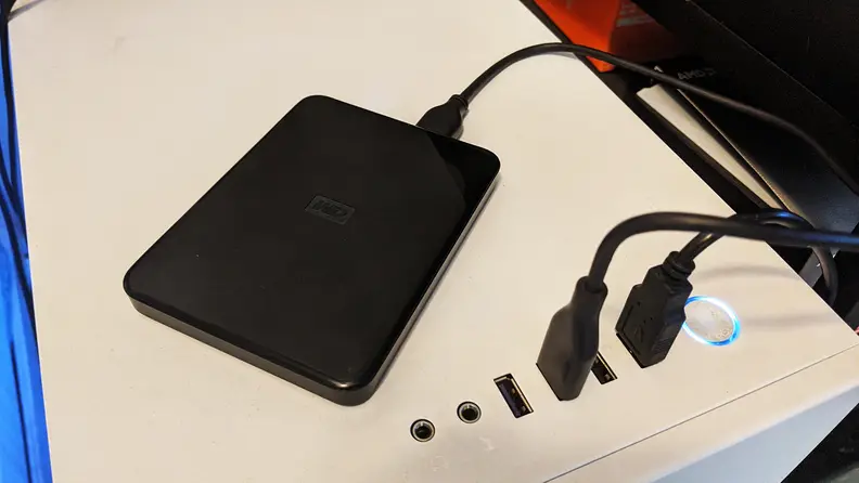 A small external hard drive plugged into the top of a desktop computer case backing files up for donation or recycling