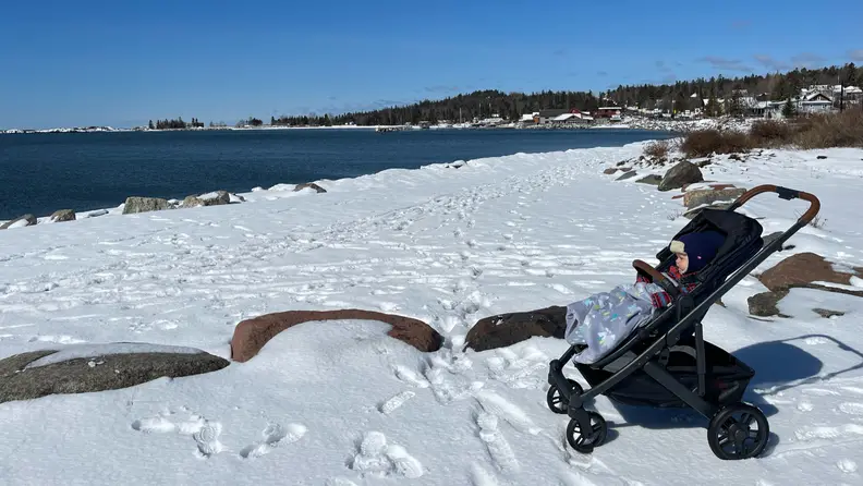 A baby in an Uppababy Cruz V2 stroller wrapped up in a blanket sitting in a snowy field.