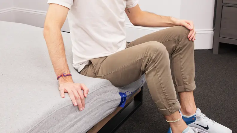 A person sitting on the edge of the mattress as the mattress itself gives out with no support.