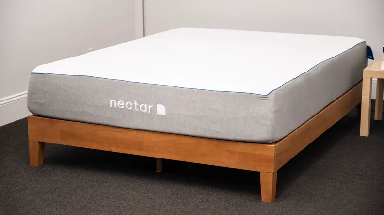 A bare Nectar mattress on a wood bed frame in a carpeted room with white walls