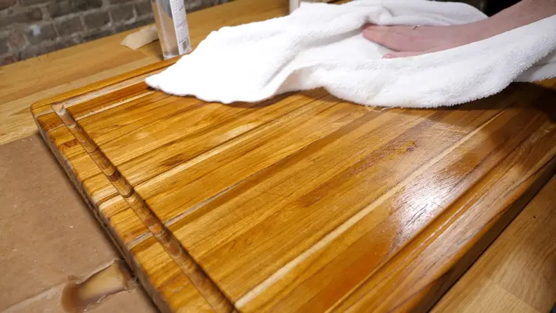 A hand wiping a wooden cutting board clean