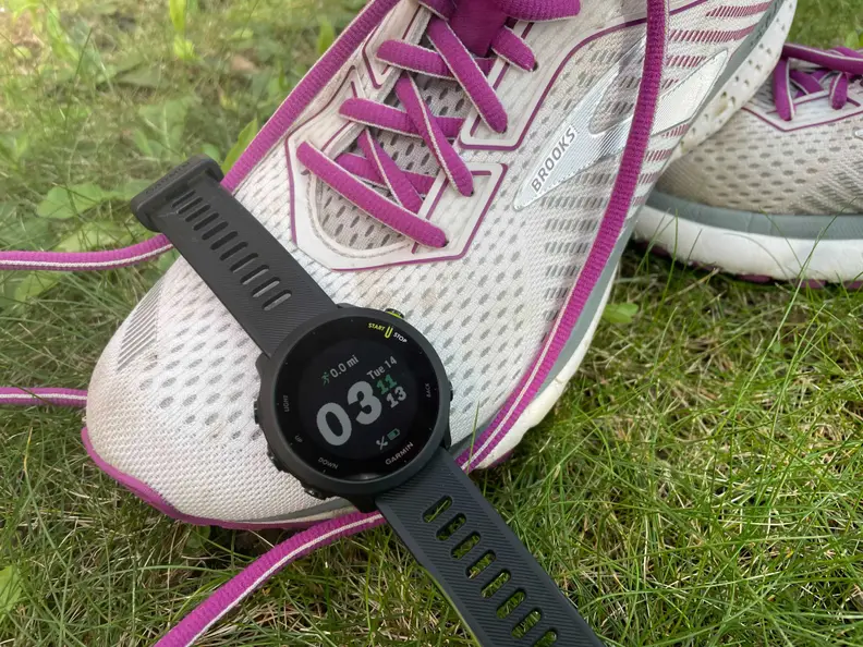 Garmin Forerunner 55 watch draped over the toe of a Brooks running shoe