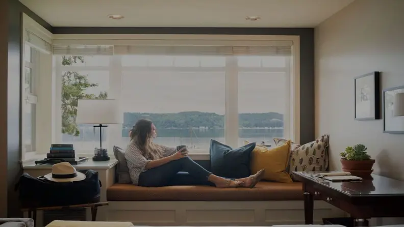 Woman looking over the window while on a sofa holding a cup