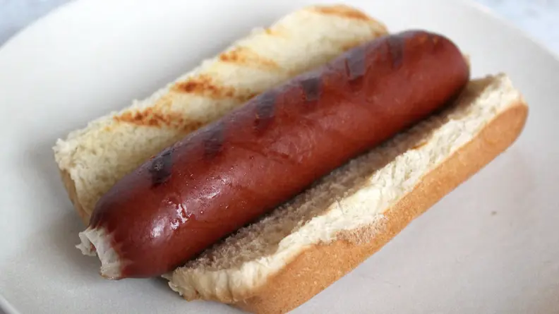 In the center of a white plate, there's Snake River Farms hot dog on a bun.