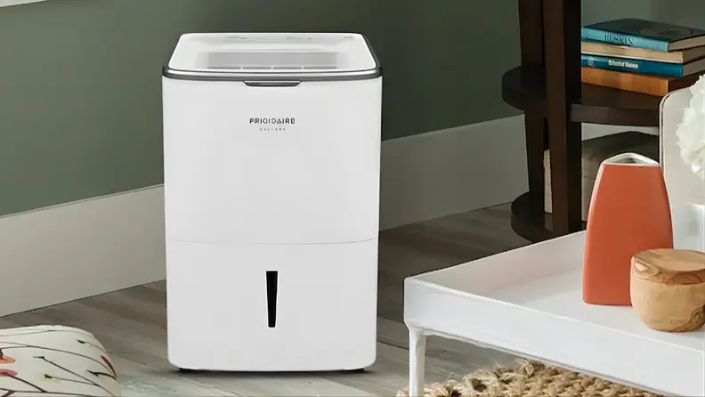 Frigidaire 50-pint smart dehumidifier standing in a living room near a table and shelving.