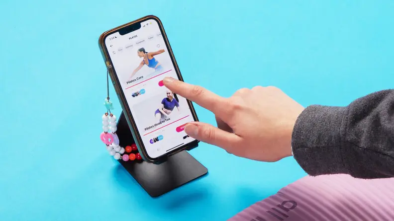 Person using finger to navigate the FitOn app on their smart phone in front of their yoga mat.