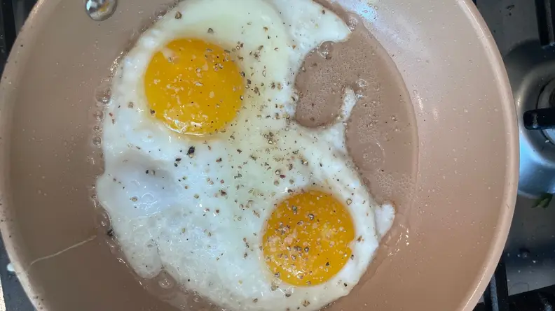 Two seasoned eggs being fried inside of nonstick skillet pan.