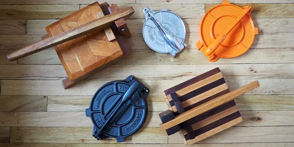Five tortilla presses laid out on a wooden background, shot from above.