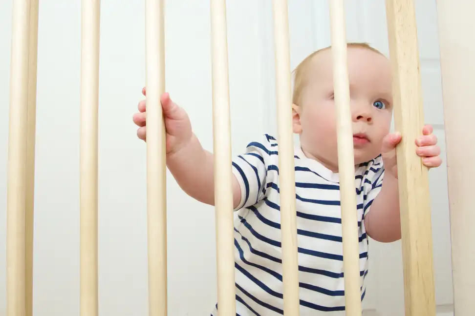 Toddler gripping the bars of a protective gate.