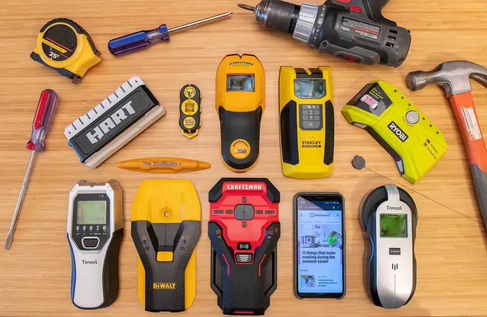An array of stud finders lined up on a wooden table, along with some other tools that form a border around them.