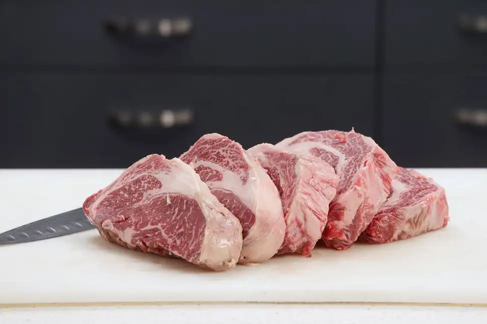 On a white cutting board, there are five thick slices of uncooked American Wagyu beef, produced by Snake River Farms.