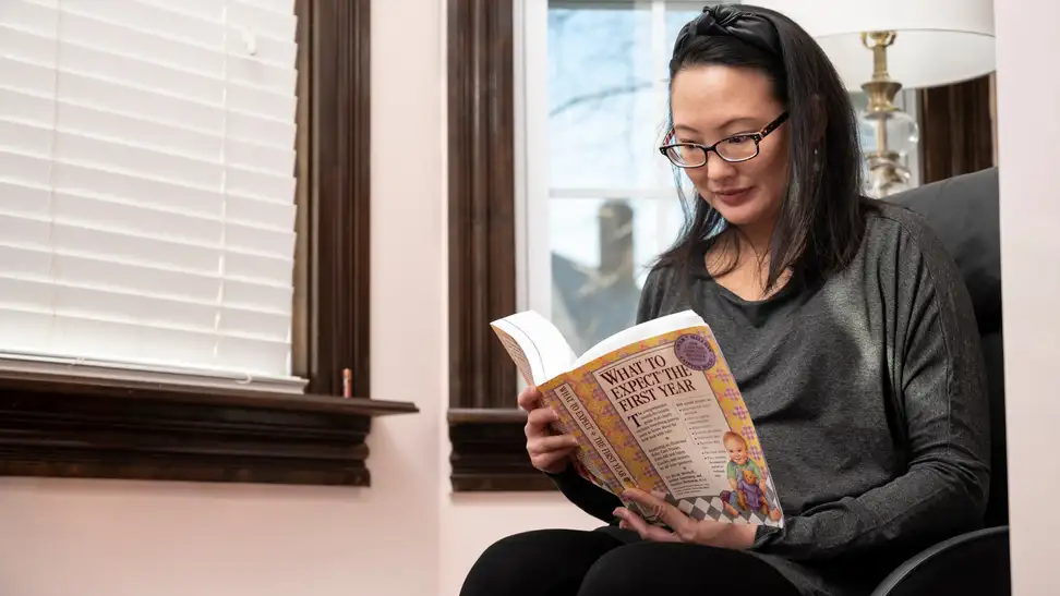 A pregnant woman reads a book about what to expect in the first year of motherhood.