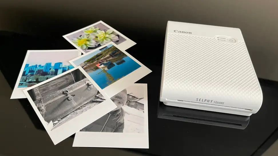 The Canon Selphy portable photo printer on a table next to some photographs.