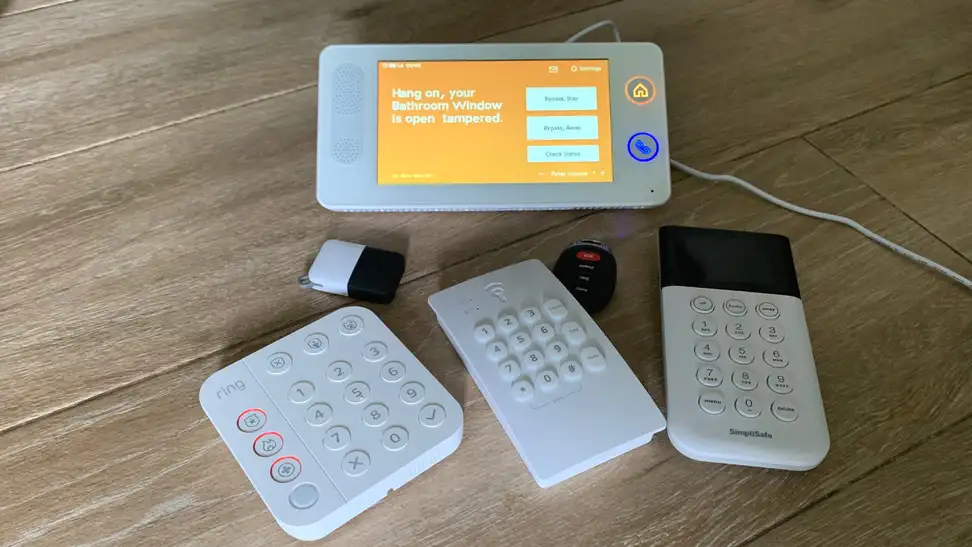 Home security system panels, keypads, and keyfobs scattered on a tile floor.