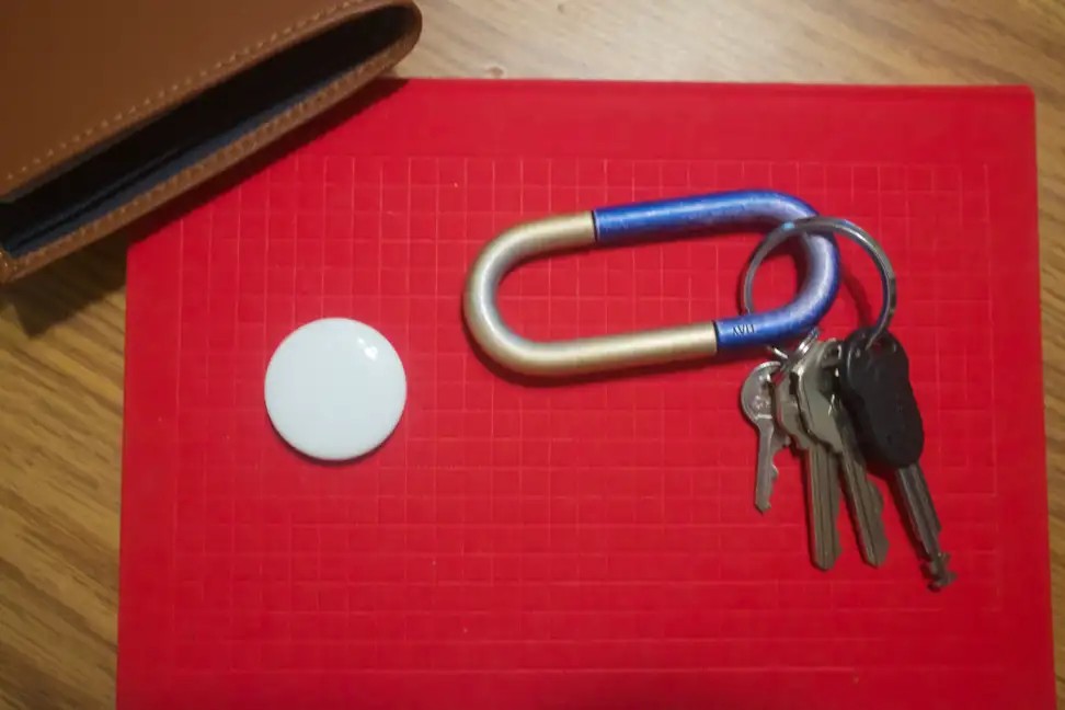 Apple's AirTag tracker, on top of a notebook, next to a wallet and set of keys.