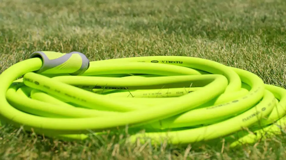 A bright green Flexzilla garden hose, coiled on a lush green lawn.