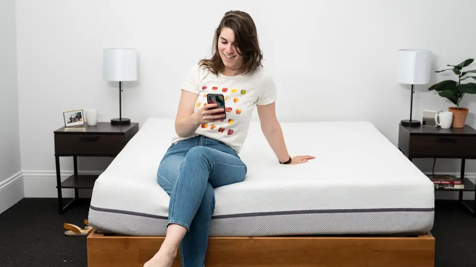a woman sits on the foot of the Purple Mattress looking at her phone.