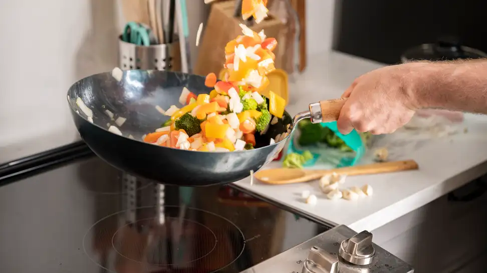 A person is stir frying a medley of vegetables in a carbon steel wok over an electric cooktop.