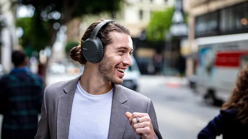 Man smiling while wearing  Sony WH-CH710N noise-canceling headphones outdoors.