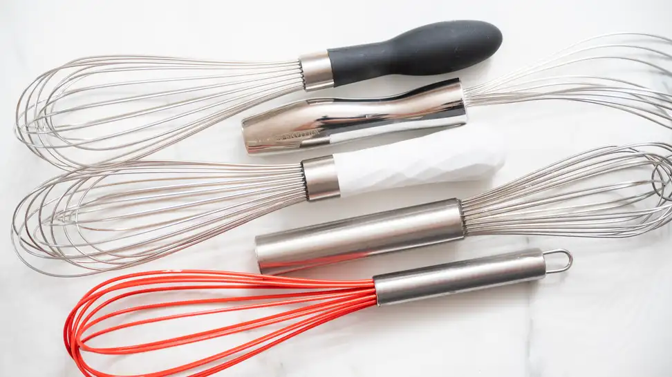 Assorted whisks arranged on a marble countertop.