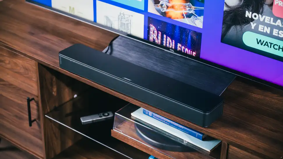 The Bose TV Speaker sits perfectly under a TV, set in all black on a rich wooden cabinet above a record player and other accessories.