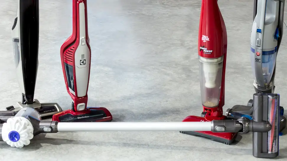 Four cordless vacuums standing side by side and one lying on its side on a grey concrete floor.