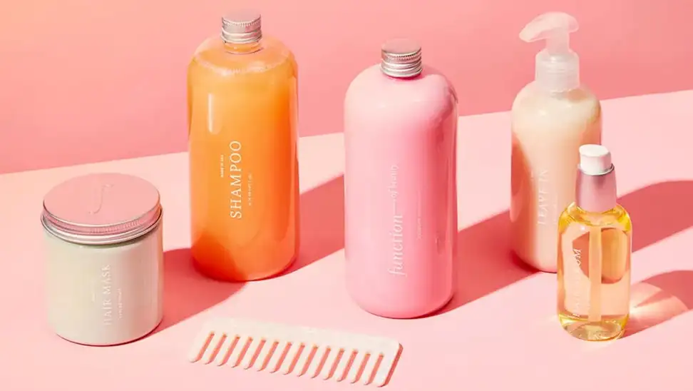 Multi-colored hair products and comb in front of pink background.