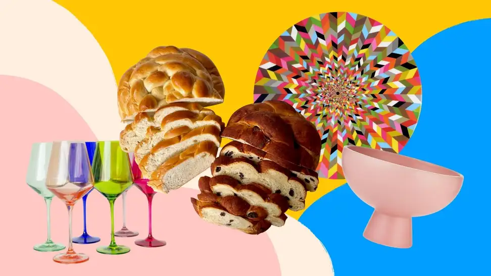 Colorful wine glasses, round challah loaves, a multicolored lazy susan, and a pink bowl arranged playfully on a colorful pink, yellow, and blue patterned background.