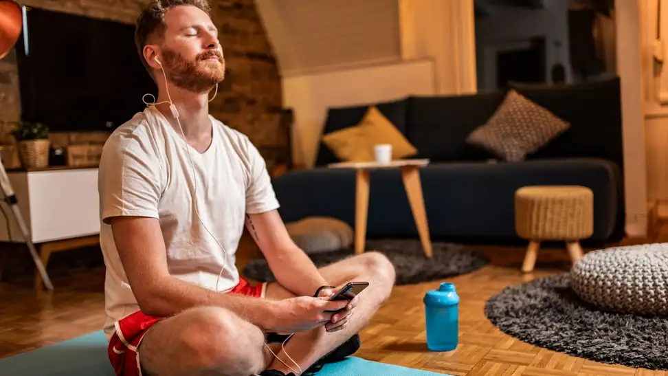 a person sits on a yoga mat holding their phone and listening to audio as though they're meditating