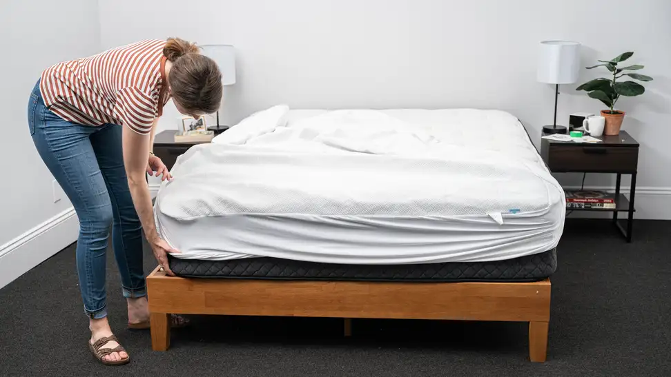 Person putting mattress protector on bed.