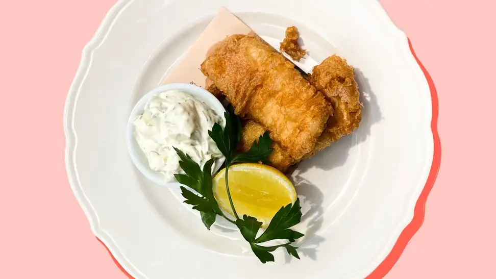 Beer-battered fried fish on a white plate accompanied by homemade tartar sauce and a lemon wedge.