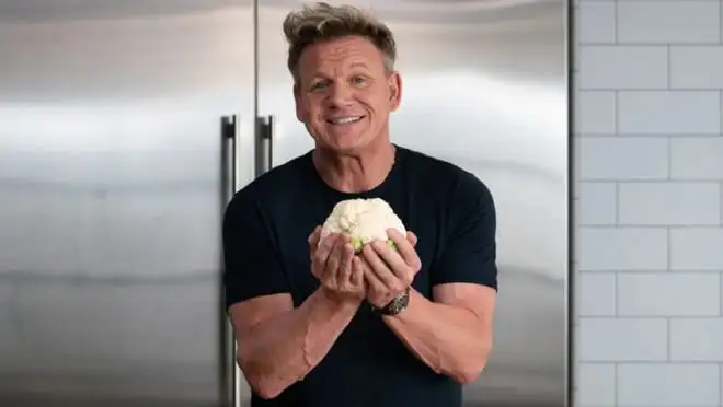 Chef Gordon Ramsay holds a clump of dough in a kitchen.