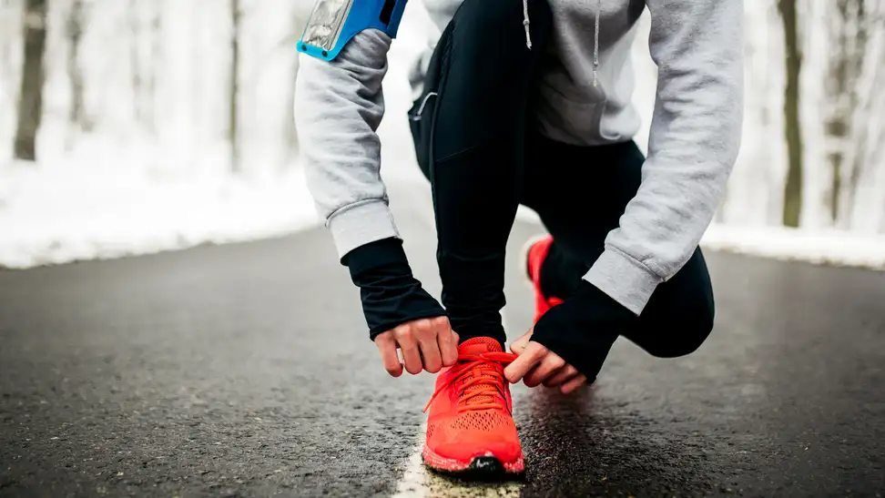 Girl bending down to tie her shoes on a winter run.