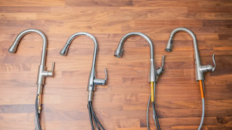 Four uninstalled kitchen faucets lay on their sides on a butcherblock counter