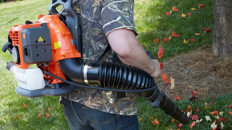 Photo of an orange Husqvarna backpack leaf blower in use outdoors.